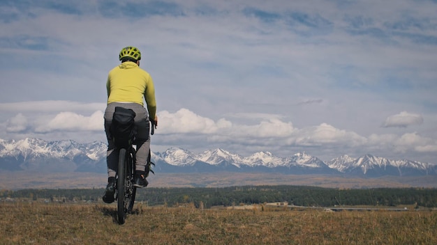 Der Mann reist auf gemischtem Gelände Radtouren mit Bikepacking Die Reise des Reisenden mit Fahrradtaschen Sporttourismus Bikepacking Fahrradsportbekleidung in grün-schwarzen Farben Berg schneebedeckt