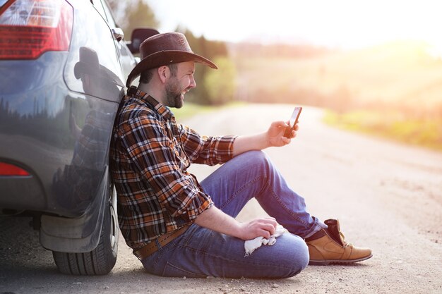 Der Mann sitzt auf der Straße beim Auto in der Natur