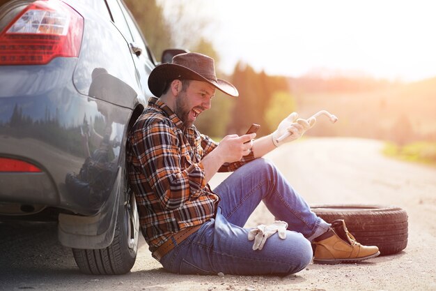 Der Mann sitzt auf der Straße beim Auto in der Natur