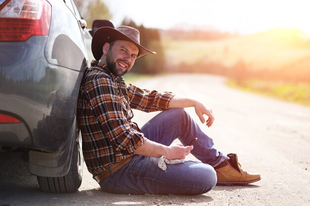 Der Mann sitzt auf der Straße beim Auto in der Natur