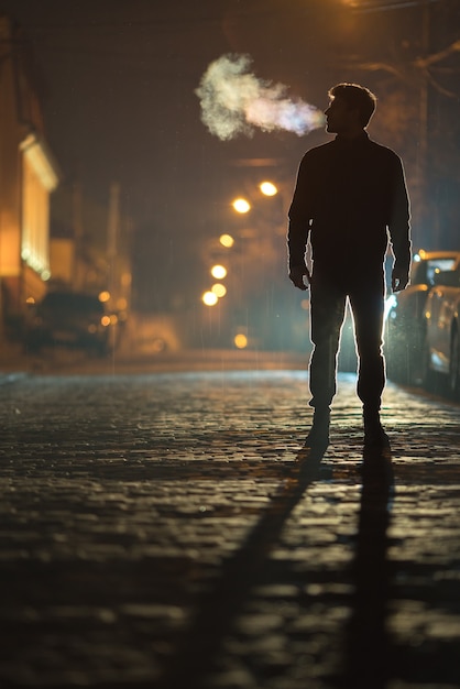 Der Mann steht auf der Regenstraße. Abend Nachtzeit. Aufnahme mit Teleobjektiv