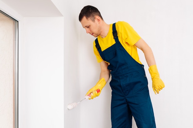 Der Mann streicht die Wände und die Decke in weißer Farbe. Malerei und Reparatur des Zimmers.