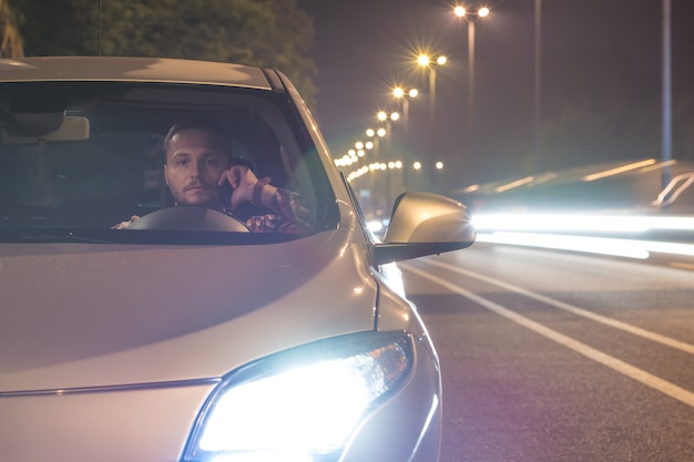 Der Mann telefoniert im Auto auf der Straße. abend nacht zeit