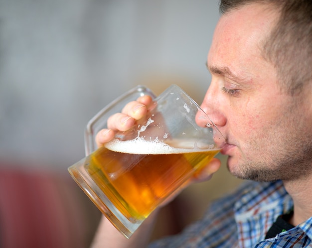 Der Mann trinkt ein frisches, kaltes alkoholisches Bier aus einem großen Becher