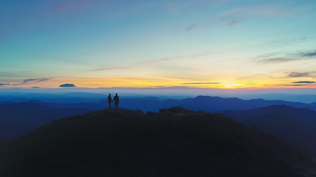 Der Mann und die Frau, die auf dem Berg auf dem Sonnenunterganghintergrund stehen