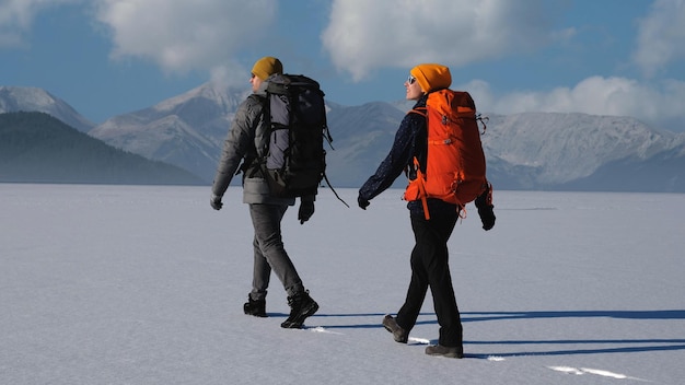 Foto der mann und die frau mit rucksäcken gehen auf einem schneebedeckten berghintergrund