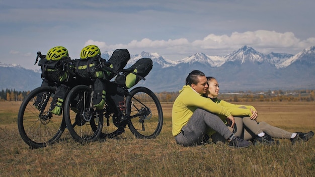Der Mann und die Frau reisen auf gemischtem Gelände Radtouren mit Bikepacking Die zwei Personen reisen mit Fahrradtaschen Sportbikepacking Fahrradsportbekleidung in grün-schwarzen Farben Berg schneebedeckt