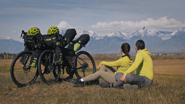 Der Mann und die Frau reisen auf gemischtem Gelände Radtouren mit Bikepacking Die zwei Personen reisen mit Fahrradtaschen Sportbikepacking Fahrradsportbekleidung in grün-schwarzen Farben Berg schneebedeckt