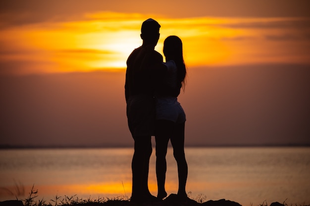 Der Mann und eine Frau, die nahe einem Wasser auf dem Sonnenunterganghintergrund stehen