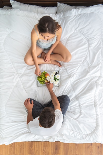 Der Mann und eine Frau frühstücken auf dem Bett. Sicht von oben