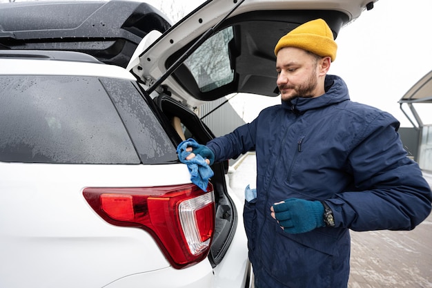 Der Mann wischt den Kofferraum eines amerikanischen SUV-Autos nach dem Waschen bei kaltem Wetter mit einem Mikrofasertuch ab