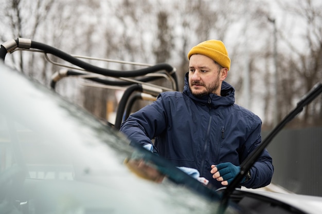 Der Mann wischt die Windschutzscheibe eines amerikanischen SUV-Autos nach dem Waschen bei kaltem Wetter mit einem Mikrofasertuch ab