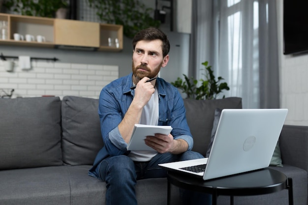 Der Mann zu Hause studiert aus der Ferne und verwendet einen Laptop, der zu Hause auf der Couch sitzt und eine Vorlesung aufzeichnet