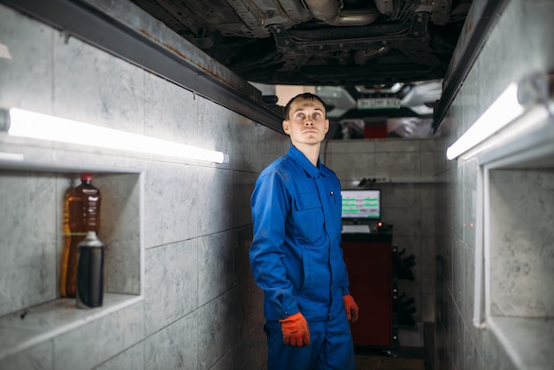 Der Mechaniker in der Grube überprüft den Boden des Autos.