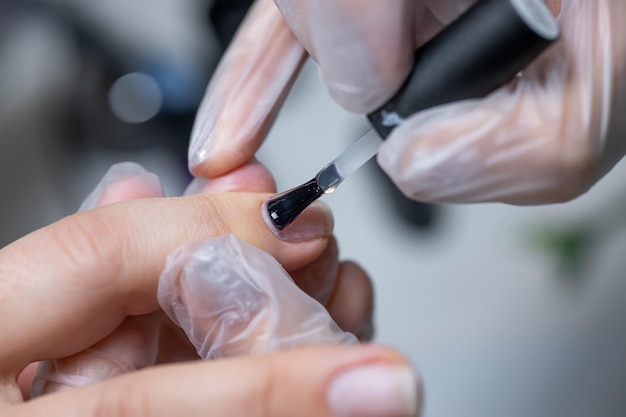 Der Meister des Nagelservices macht eine Maniküre, um das Gel mit einem Pinsel auf den behandelten Nagel aufzutragen