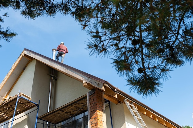 Der Meister für die Installation von Lüftungsrohren und die Installation des Schornsteins des Ofens arbeitet auf dem Dach des Hauses