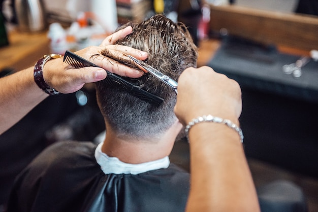 Der Meister im Friseursalon rasiert und schneidet den Mann vor dem Spiegel