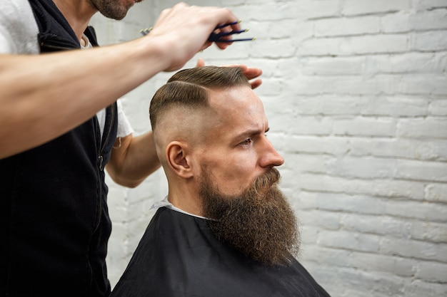 Der Meister schneidet im Friseursalon Haare und Bart des Menschen