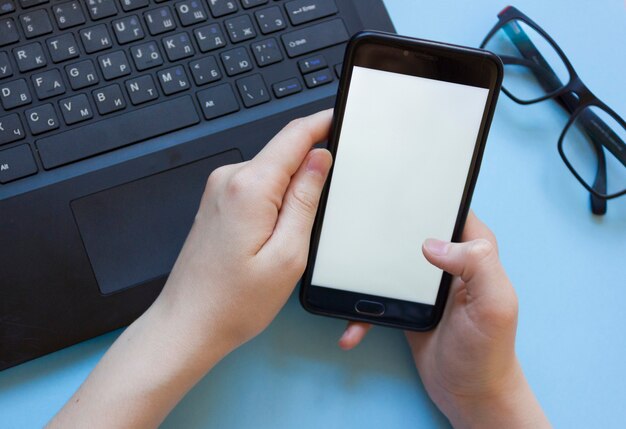 Der Mensch arbeitet an einem Laptop und hält ein Telefon flach in der Hand. Das Problem der Konzentration bei der Arbeit während der Arbeit von zu Hause aus. Der Mann wird durch das Telefon abgelenkt, während er von zu Hause aus am Laptop arbeitet.