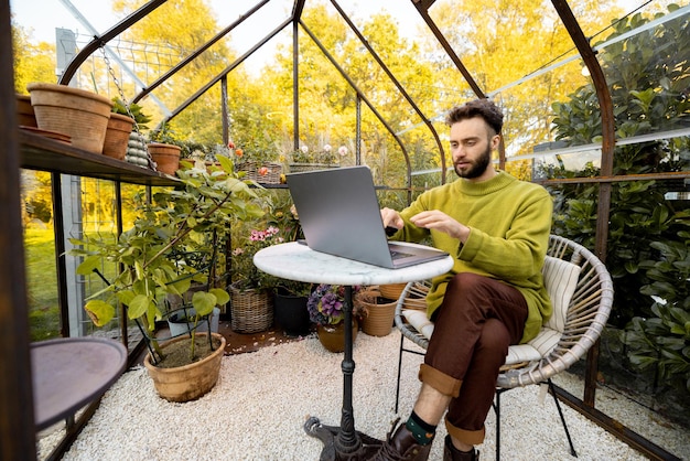 Der Mensch arbeitet aus der Ferne am Laptop im Gewächshaus im Hinterhof