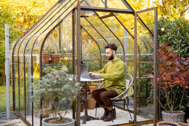 Der Mensch arbeitet aus der Ferne am Laptop im Gewächshaus im Hinterhof