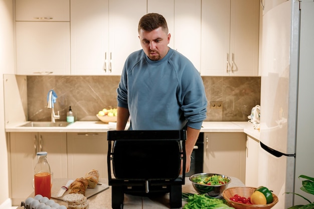 Der Mensch bereitet köstliches saftiges Fleischsteak auf einem Elektrogrill auf einem Holztisch zu Rauch in der heimischen Küche