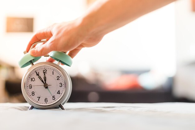 Der Mensch drückt einen Wecker in der Morgensonne und im verschwommenen Hintergrund