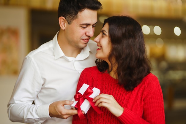 Der Mensch gibt seiner Frau eine Geschenkbox mit rotem Band Ein liebevolles Paar, das den Valentinstag feiert