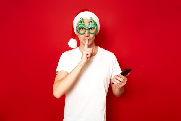 Der Mensch legte den Finger auf die Lippen, Zeichen der Stille, Geheimhaltung, Geheiminformationen, die das Telefon in der Hand hielt