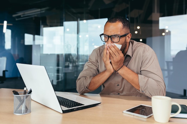 Der Mensch niest und hat eine laufende Nase im Büro bei der Arbeit afroamerikanischer Geschäftsmann krank, der drinnen arbeitet