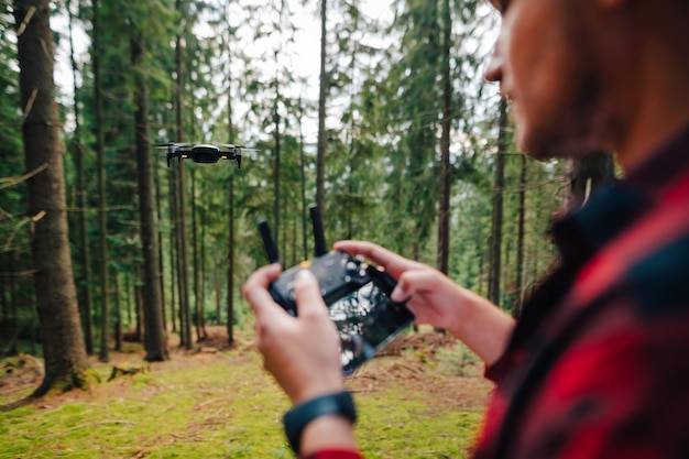 Der Mensch steuert eine Drohne von einer Fernbedienung im Wald aus und konzentriert sich auf eine Drohne im Flug