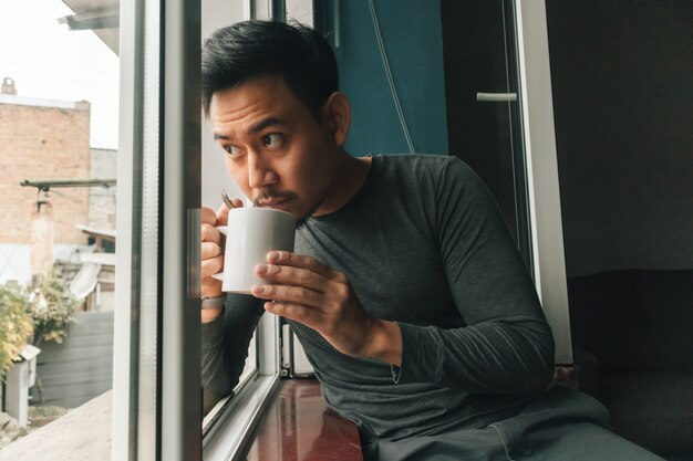 Der Mensch trinkt heißen Kaffee und fühlt sich am Fenster entspannt.