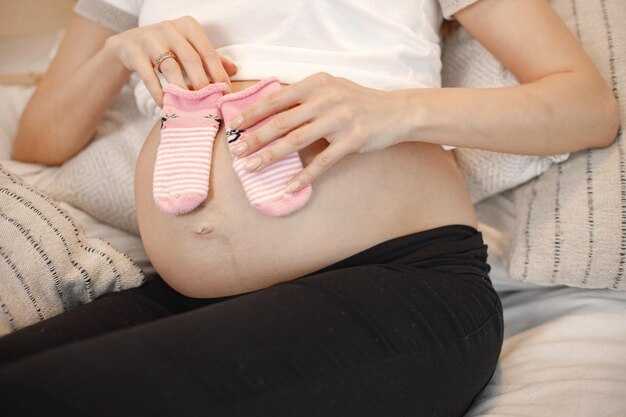 Der Mittelteil der schwangeren Frau liegt auf einem Bett und hält kleine Babysocken