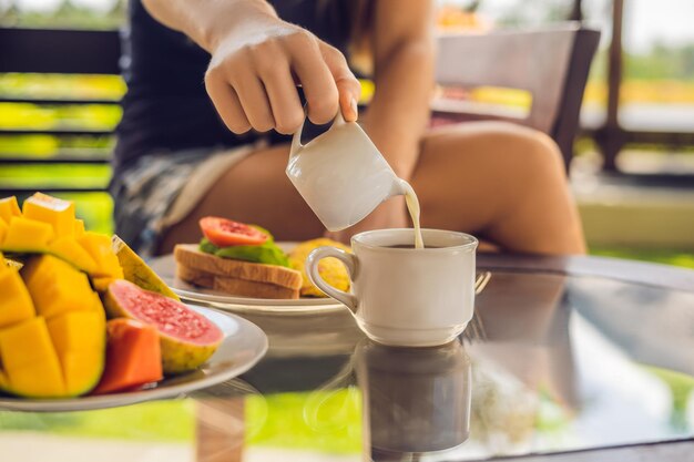 Der Moment, in dem Milch in Kaffee gegossen wird. Frau gießt Sahne in Kaffee.