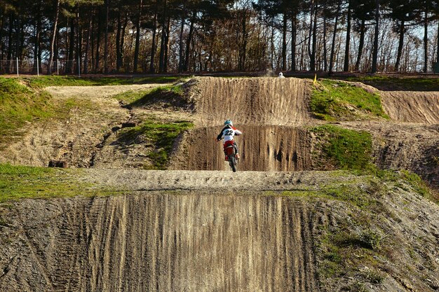 Der Motocross-Fahrer beschleunigt das Motorrad und springt auf das Sprungbrett des Rennens