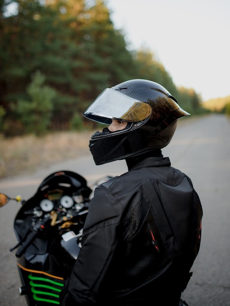Der Motorradfahrer schaut mit einem halboffenen Helm zur Seite. Motorradfahrer im Lederanzug allein auf dem Motorrad