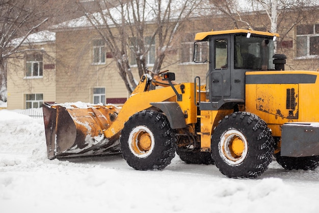 Der orangefarbene Traktor räumt Schnee von der Straße und lädt ihn in den LKW. Reinigung der Straßen in der Stadt