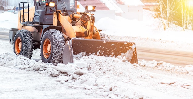 Der orangefarbene Traktor räumt Schnee von der Straße und lädt ihn in den LKW. Reinigung von Straßen