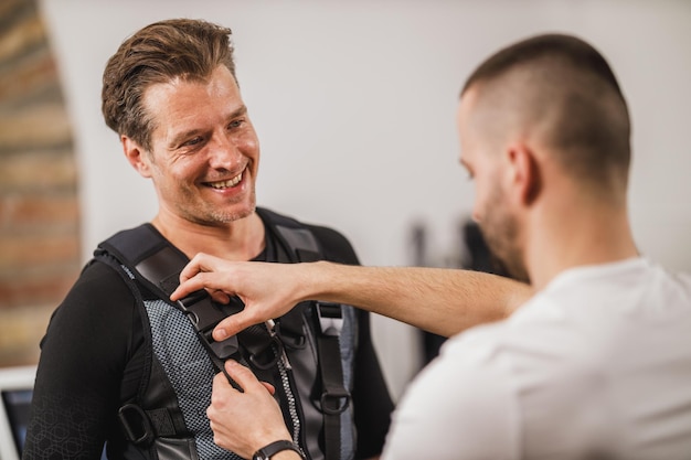 Der Personal Trainer hilft einem Mann mittleren Alters mit einem Anzug für das EMS-Training im Fitnessstudio.