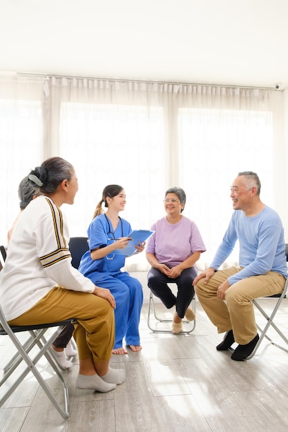 Der Pflegetherapeut sitzt mit einer Gruppe asiatischer Senioren im Kreis.