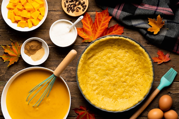 Der Prozess der Herstellung von amerikanischem Kürbiskuchen auf einem Holztisch mit Zutaten, Herbstnahrungsmittelzusammensetzung.