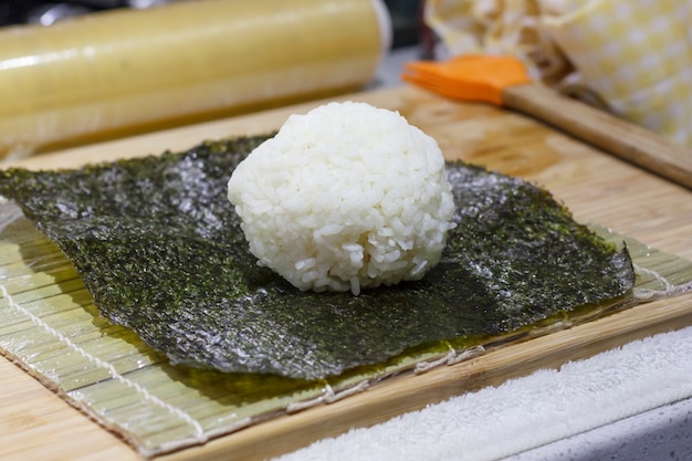 Der Prozess der Herstellung von Sushi und Brötchen mit Gurke. Reis auf Noriblatt