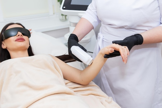 Der Prozess der Laser-Haarentfernung des weiblichen Körpers professionelle Kosmetologie Epilation der Handzone Mädchen in Schutzbrillen Körperpflegekonzept