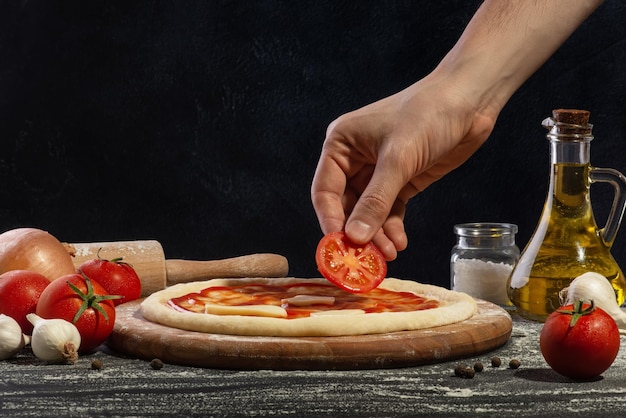 Der Prozess der Pizzaherstellung Die Hand eines Mannes legt eine Tomate auf eine Pizza