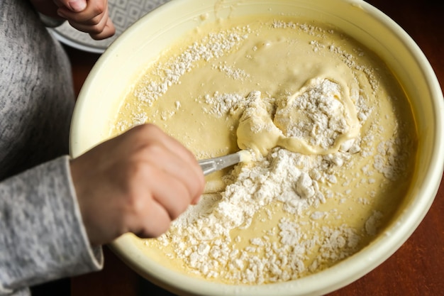 Foto der prozess der teigherstellung mit den händen eines kindes in einem gelben zeh mit einem löffel auf einem dunklen holztisch in großaufnahme