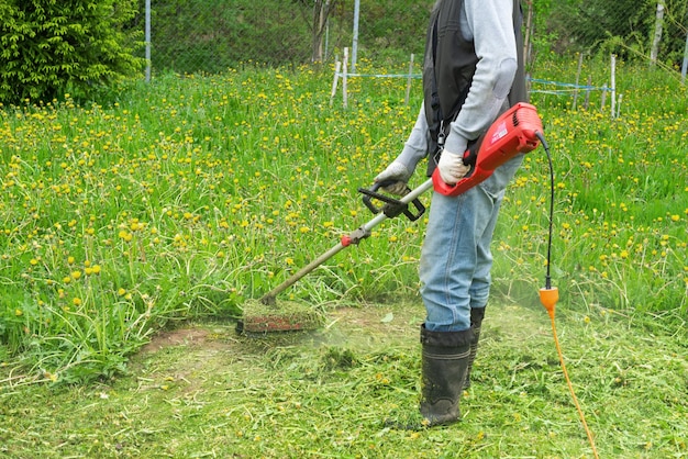 Der Prozess des Mähens von Gras mit einem Trimmer im Hof eines Landhauses