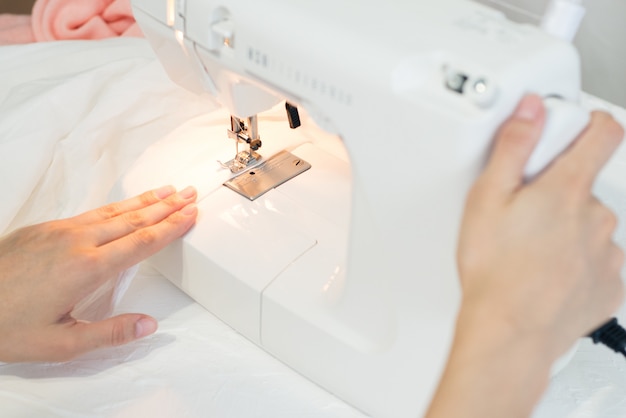 der Prozess des Nähens von Kleidung, Hände auf Nähmaschine, Nähen von weißem Stoff