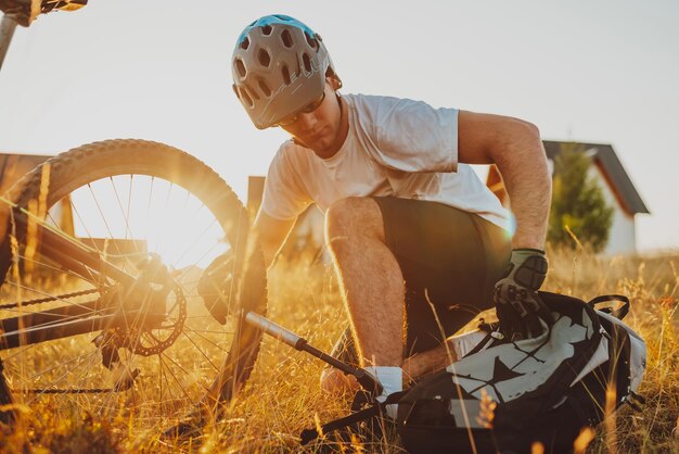 Der Radfahrer repariert und wechselt bei Sonnenuntergang den Reifen auf seinem Fahrrad zum Berg. Reparatur von Fahrradreifen. Selektiver Fokus. Hochwertiges Foto