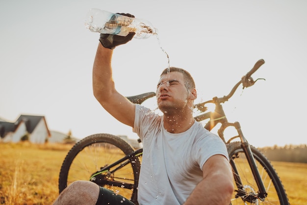 Der Radfahrer sitzt auf einer Wiese, während er sich von einer anstrengenden Fahrt auf Bergstraßen ausruht Der Radfahrer wird durch Wasser gekühlt Selektiver Fokus Hochwertiges Foto