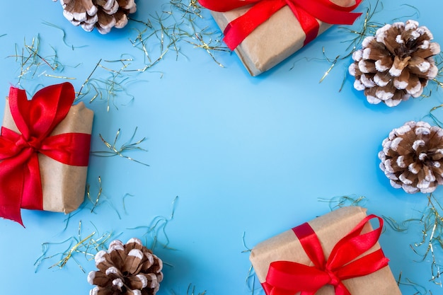 Der Rahmen von Weihnachtsschmuck-Geschenkboxen mit roten Schleifen, Tannenzapfen auf blauem Hintergrund.